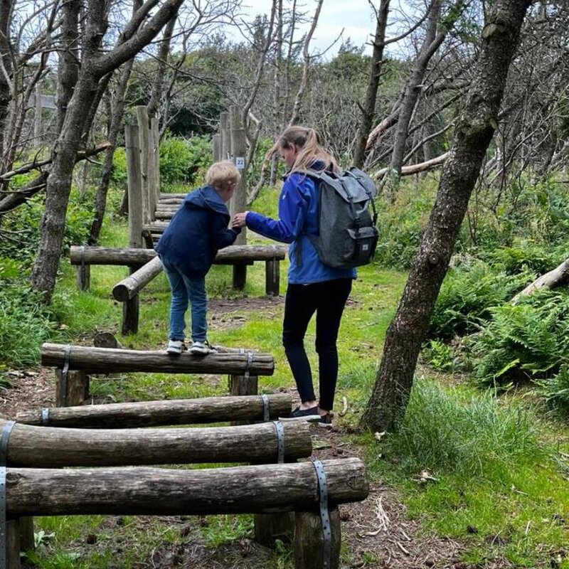 Katrin Scheffler balanciert mit ihrem Kind über Holzstämme auf einem Waldpfad